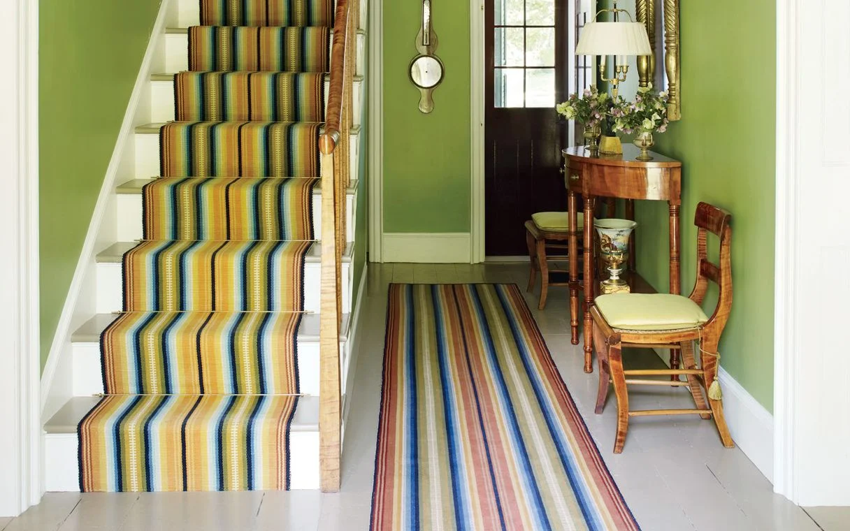 Entryway and staircase with striped runner rugs on them.