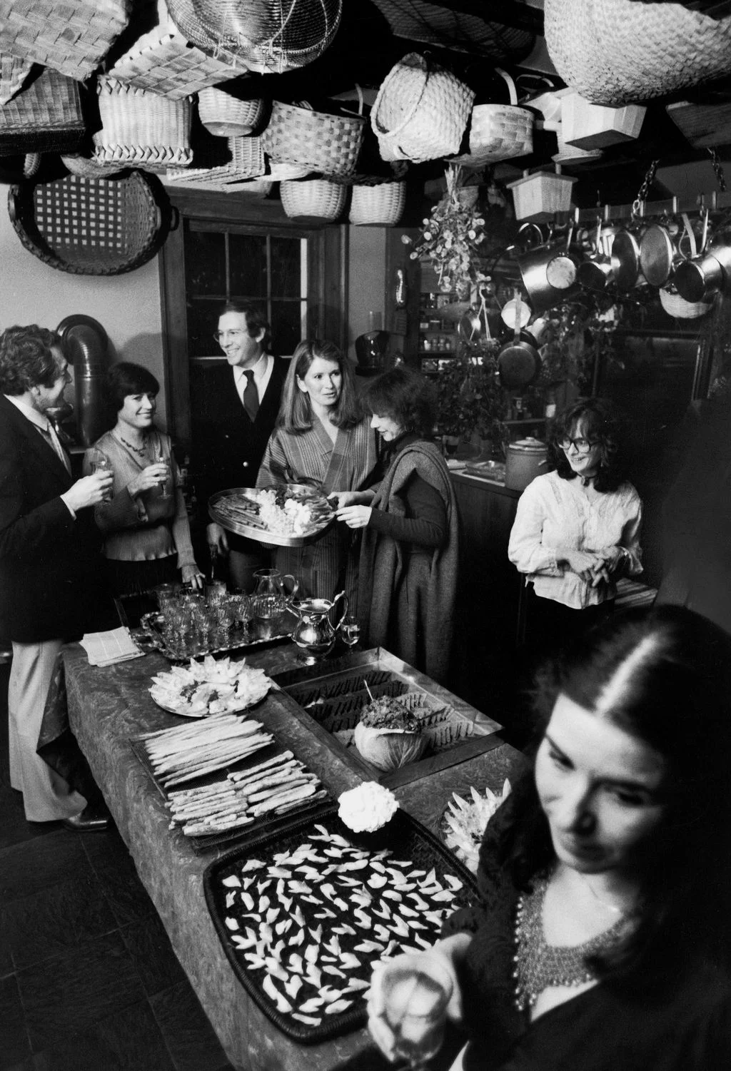 blackandwhite image of Martha Stewart offering platter of canapes to guest table in foreground set with dishes of food...