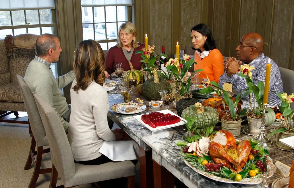 Martha Stewart seated at head of Thanksgiving table lined with many platters of food and candles Ann Curry to her right...