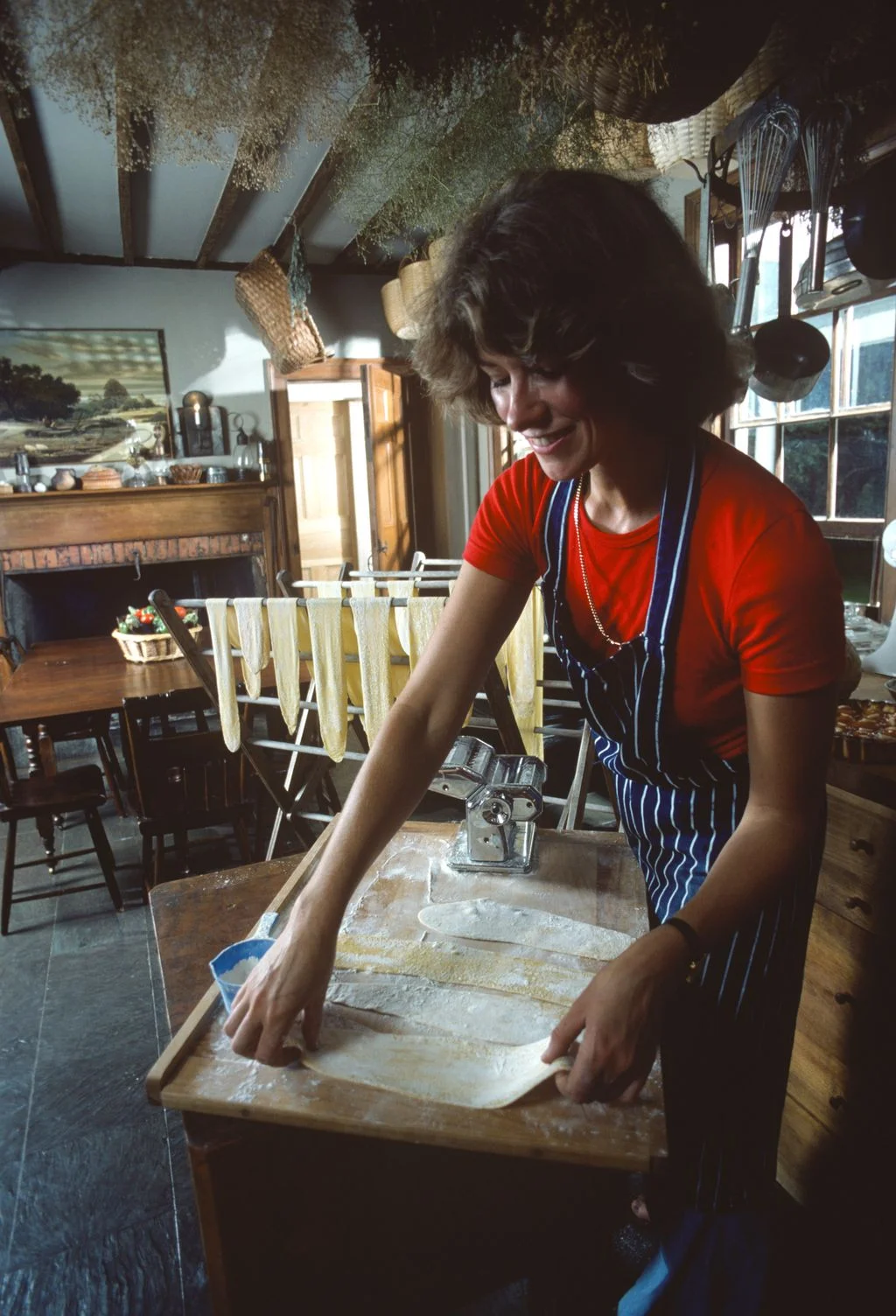 Martha Stewart in red shirt and blueandwhite striped apron lying rolled out pasta on floured wood surface in kitchen...
