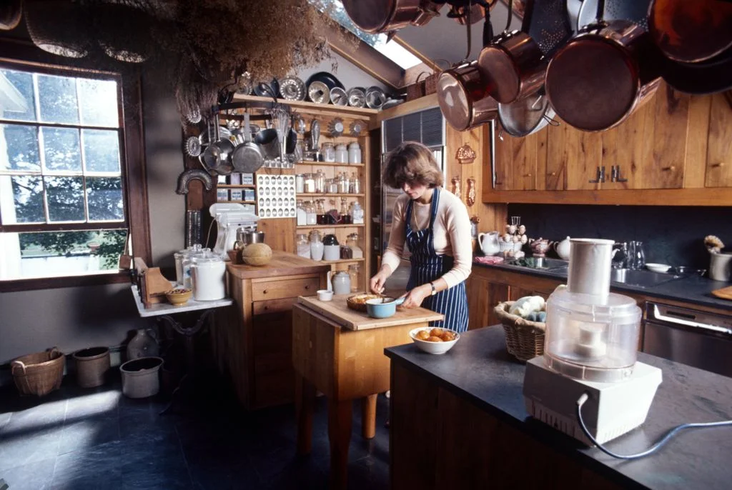 Martha Stewart standing in kitchen preparing meal at cutting board wood upper and lower cabinetry copper pots and pans...