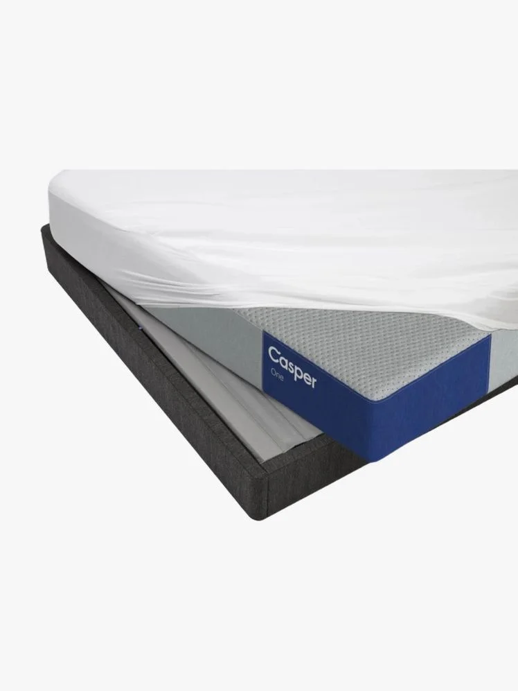 Casper mattress with a fitted sheet partially on it displayed on a bed frame.