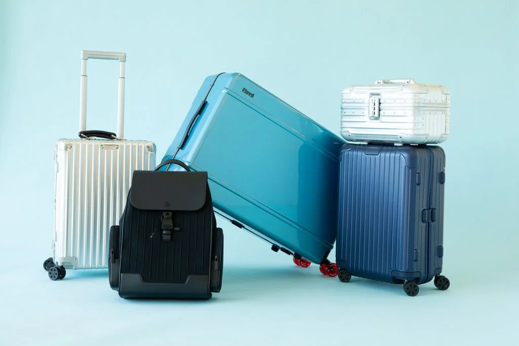 Assortment of Rimowa and Floyd hardsided suitcases and luggage against a blue background.