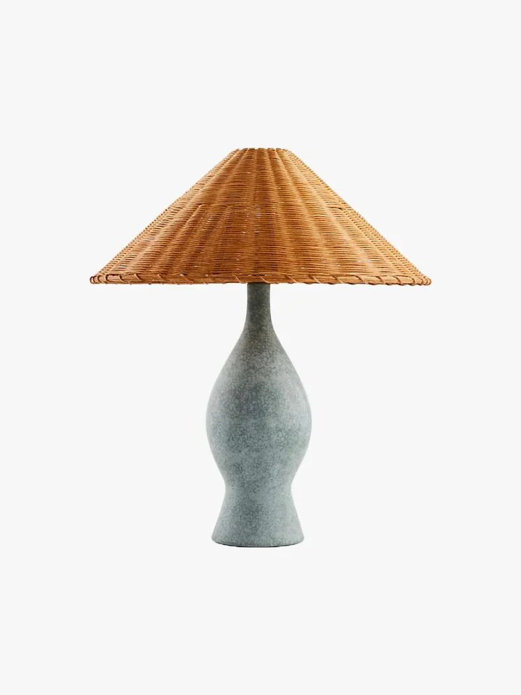 Table lamp with bottle-shaped with reactive glaze in a matte rustic green and an angled taper shade woven out of natural rattan.