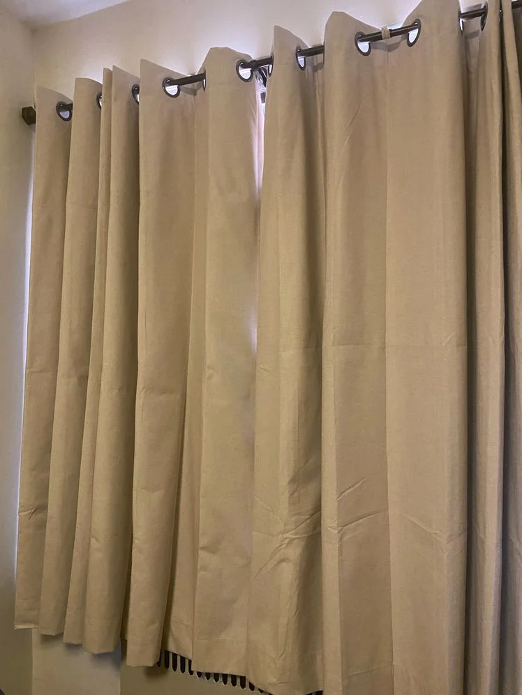 Beige blackout curtains hanging from a rod in front of a window.