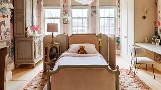 Children's room with pink floral wallpaper and a vintage bed with a folding screen behind the headboard.