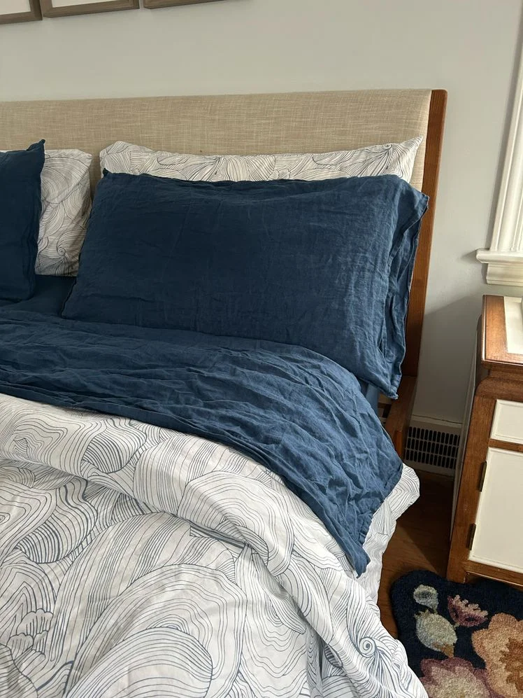 Bed made with navy blue sheets and a white patterned duvet.