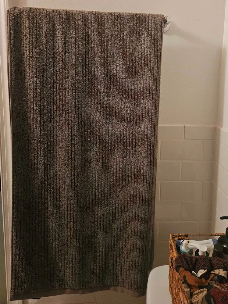 Gray bath towel hanging from a towel rod in a bathroom.