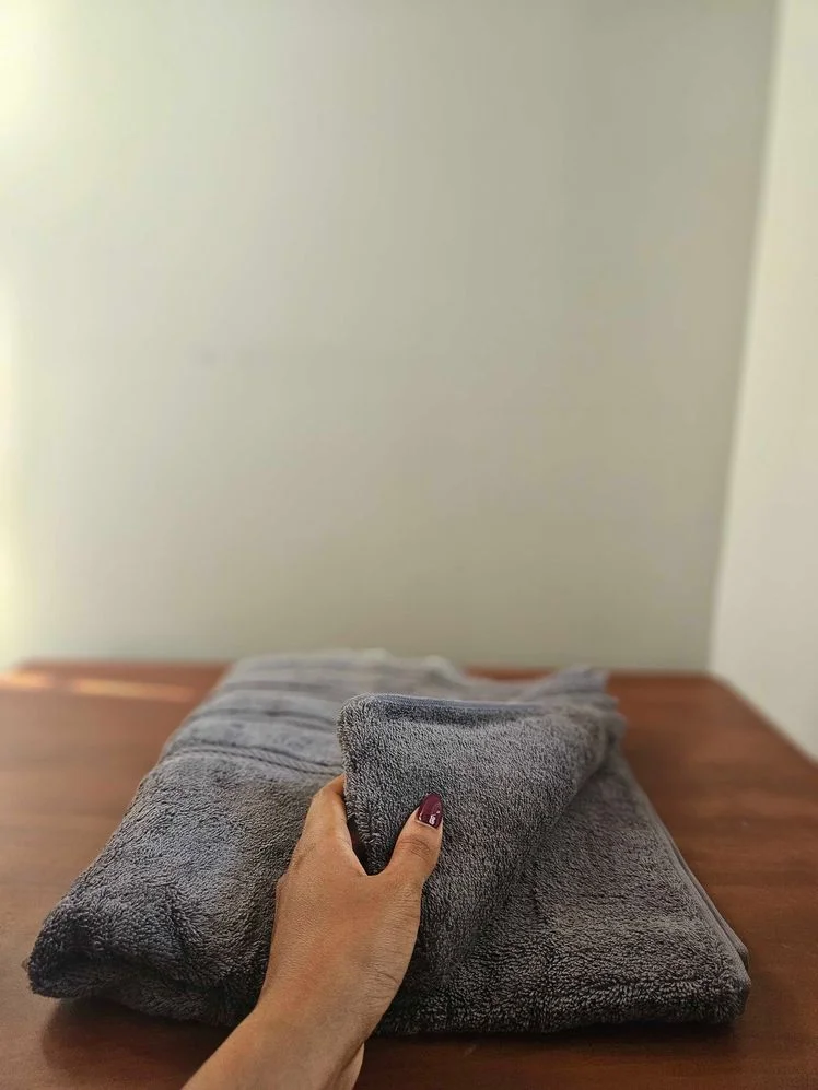 Person's hand pulling up a corner of a gray bath towel to display its texture.