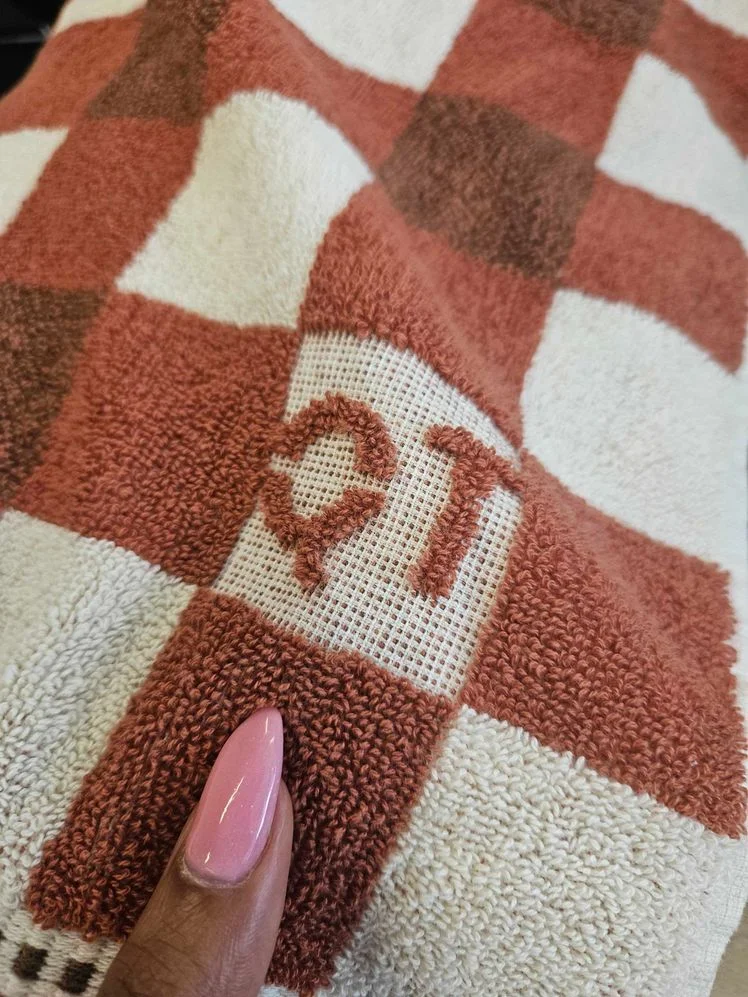 Person's hand holding a bath towel with brown checkered design to show it's texture.