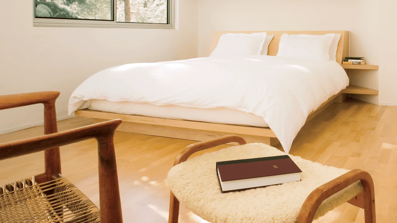 Minimalist bedroom with white comforter and pillows on a wood platform bed.