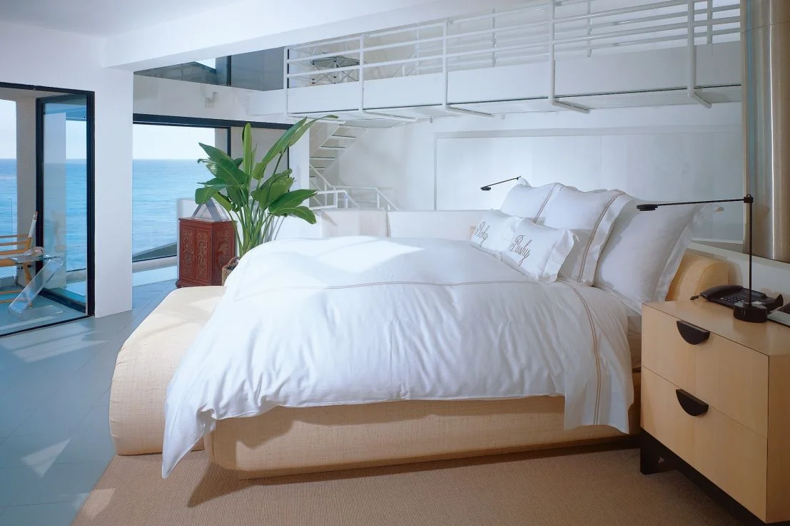 Bed made with white linens in a bedroom with a lofted space above it.