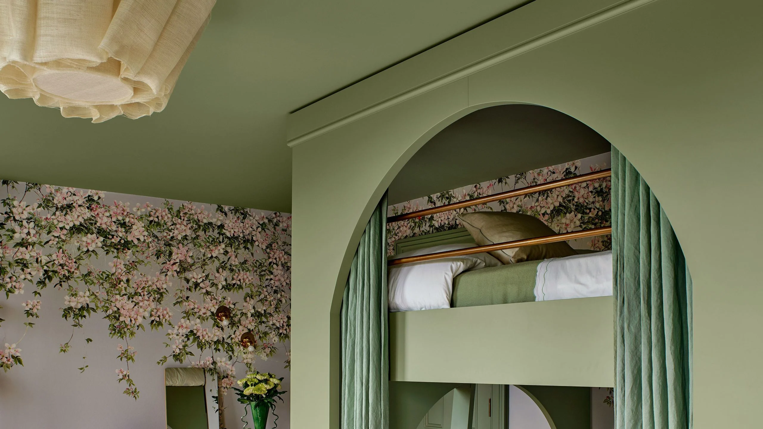 Green builtin bunk beds with arched cutouts and curtains in a bedroom with floral wallpaper.