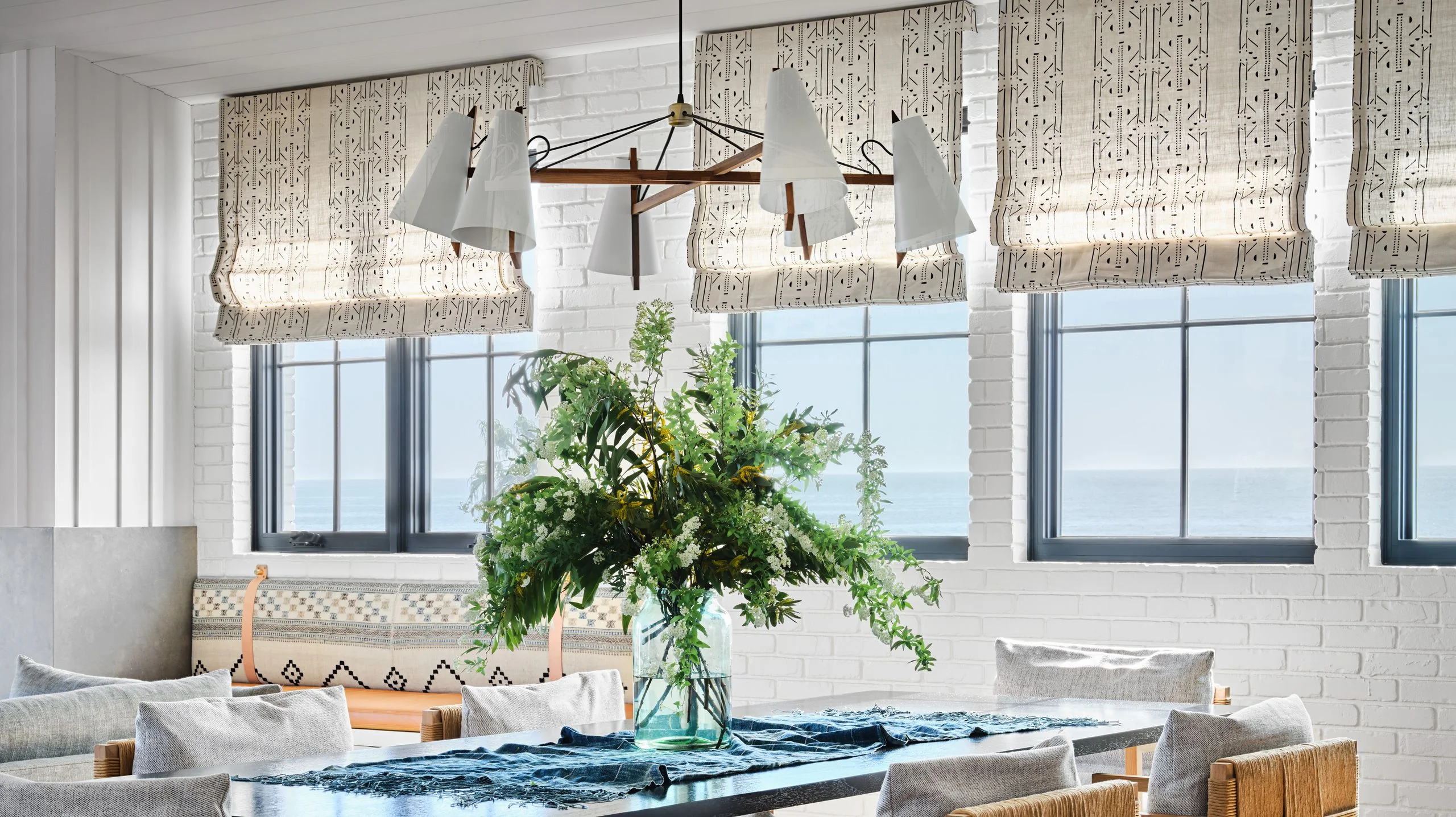Dining room in room with assorted white patterned roman shades.
