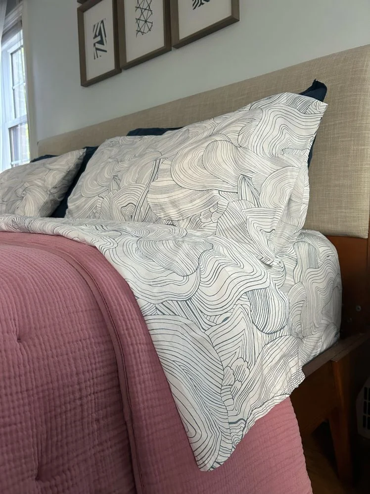 Bed made with blue and white sheets patterned like oyster shells.