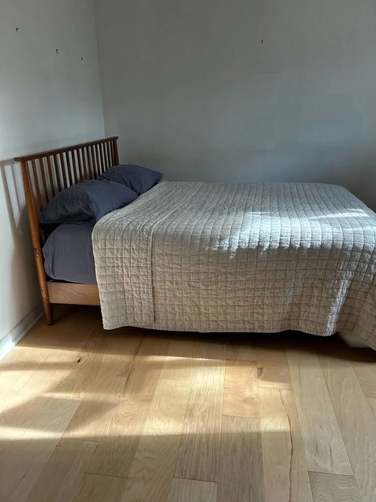 Bed on a wooden frame made with dark sheets and a beige quilt.