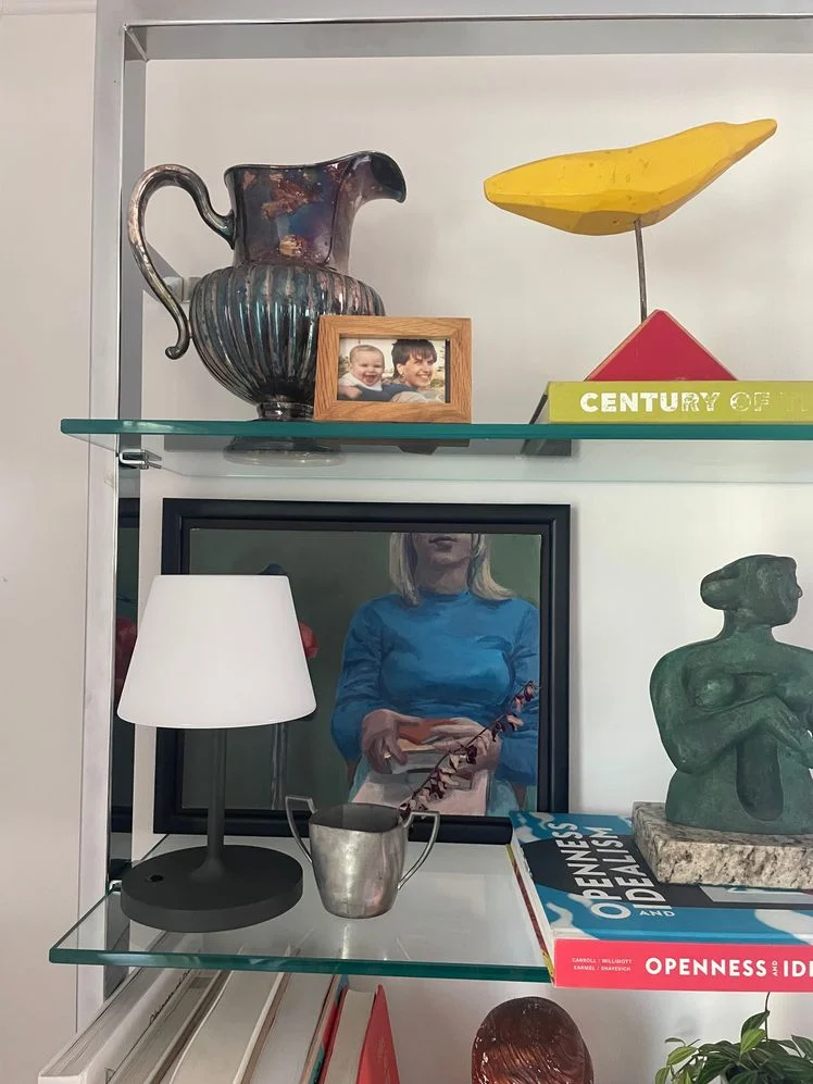 Closeup of a bookshelf with a chrome frame and glass shelves styled with various books, sculptures, and art.