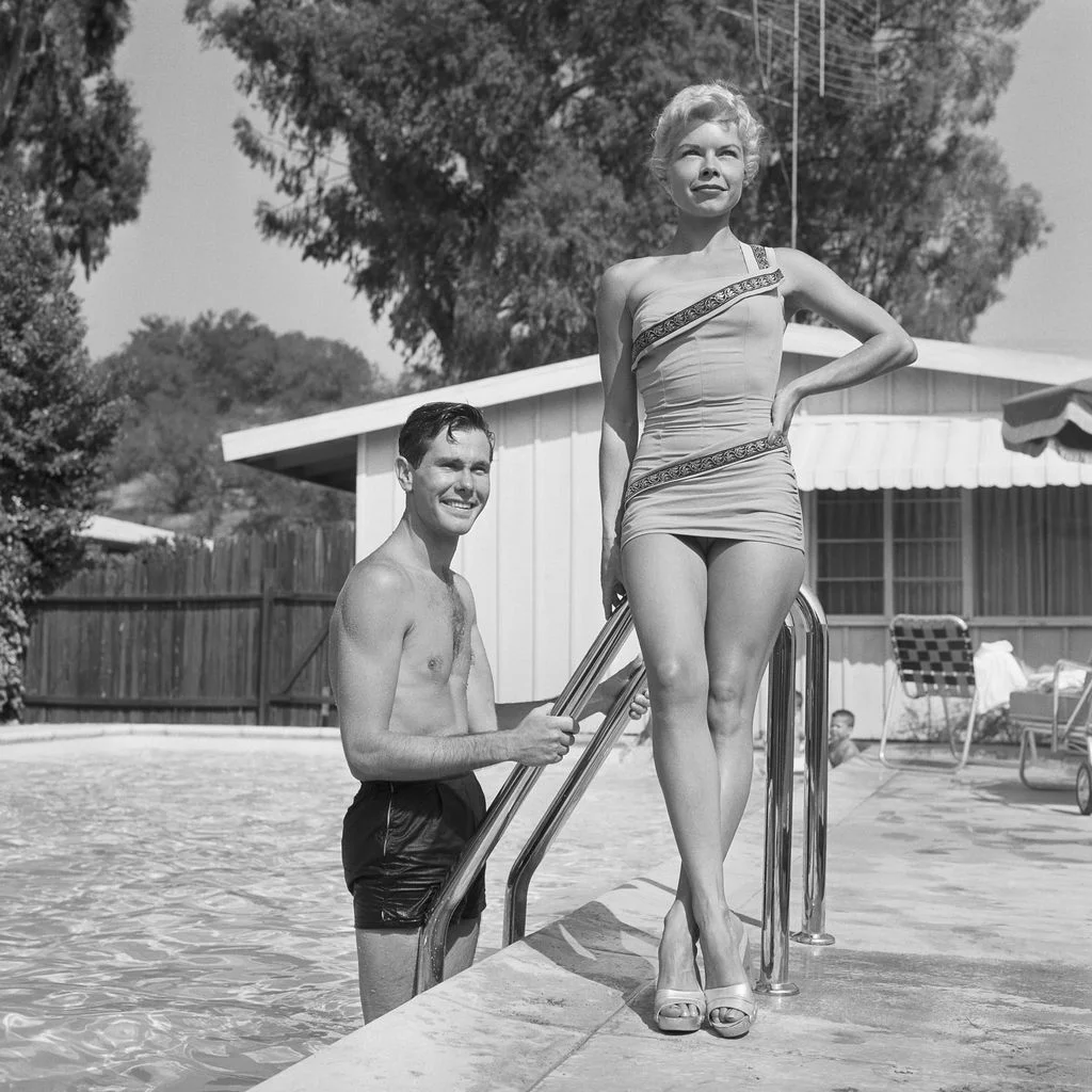 blackandwhite photo of Johnny Carson in swimming pool ascending ladder wife Jody posed poolside with hand on hip