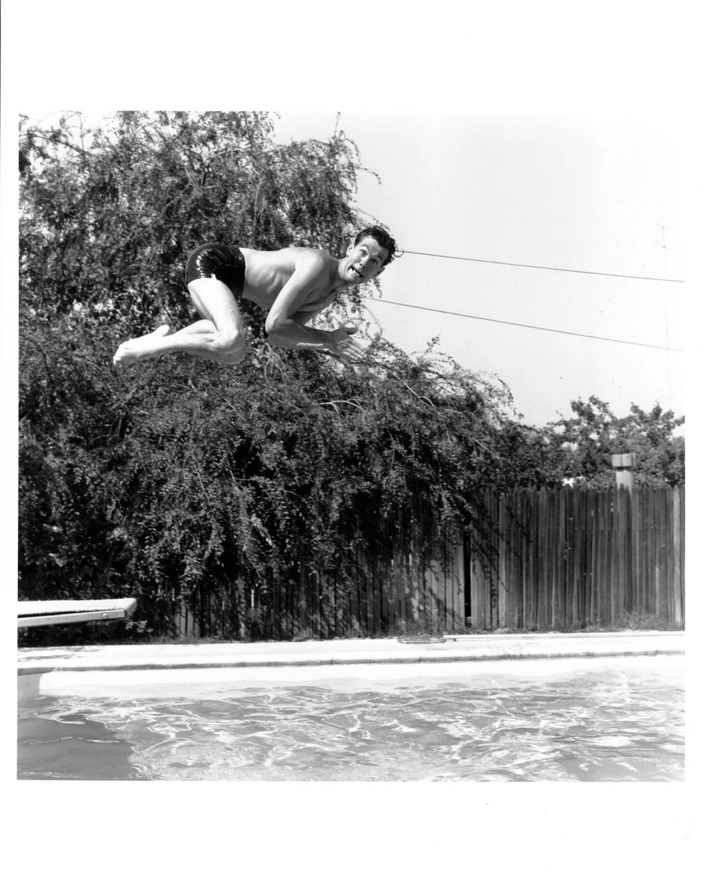 blackandwhite photo of Johnny Carson pulling a funny face while diving into his swimming pool