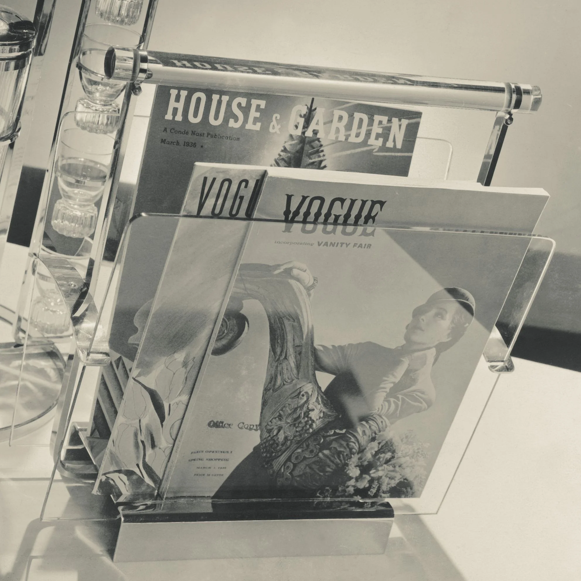 Black and white photo of a drink rack next to a magazine rack.