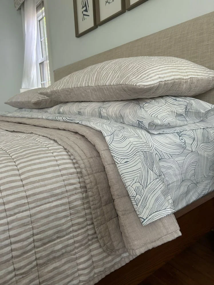 Bed made with striped quilt and patterned white sheets.