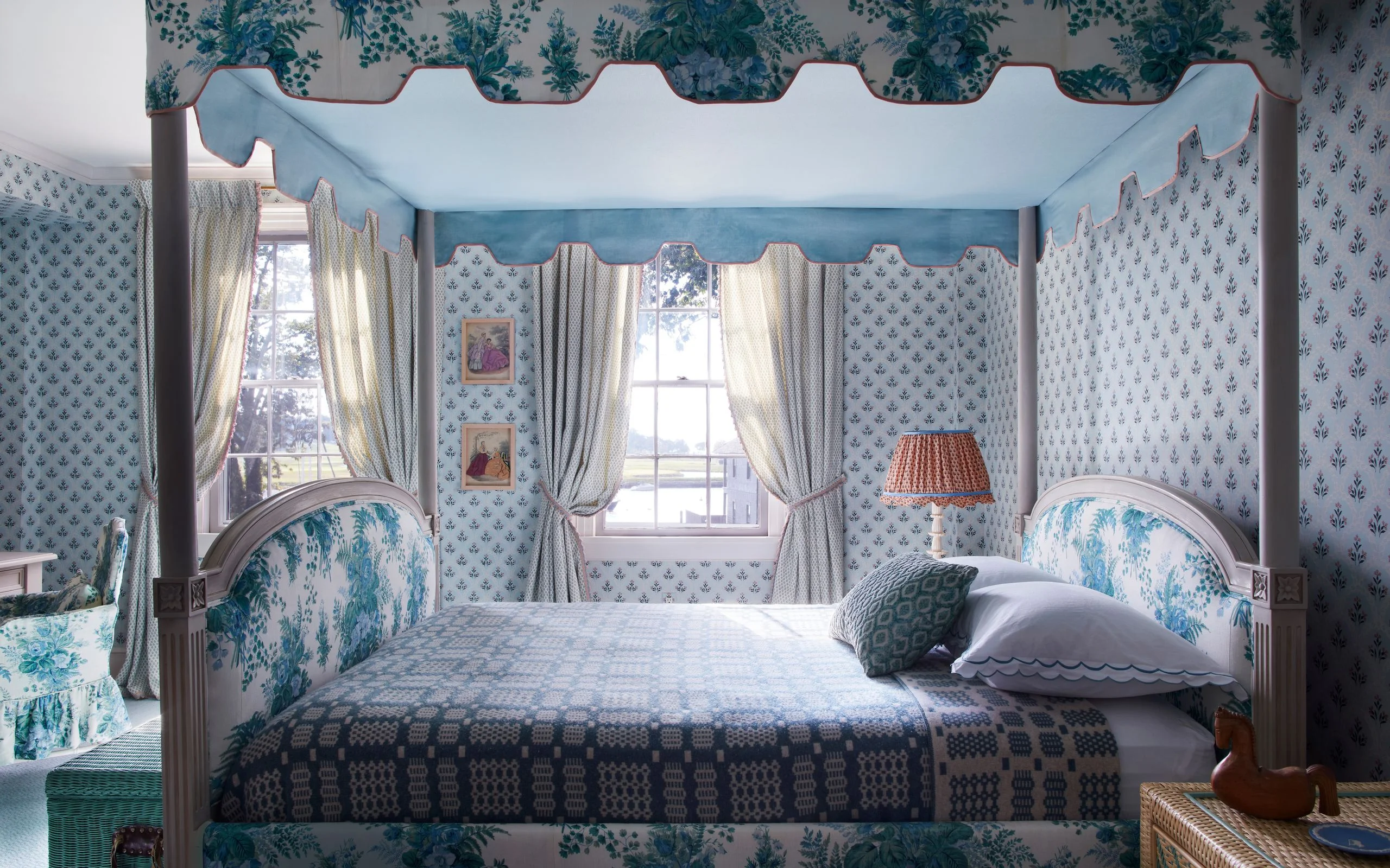 Four poster canopy bed upholstered with floral fabric in a wallpapered room.
