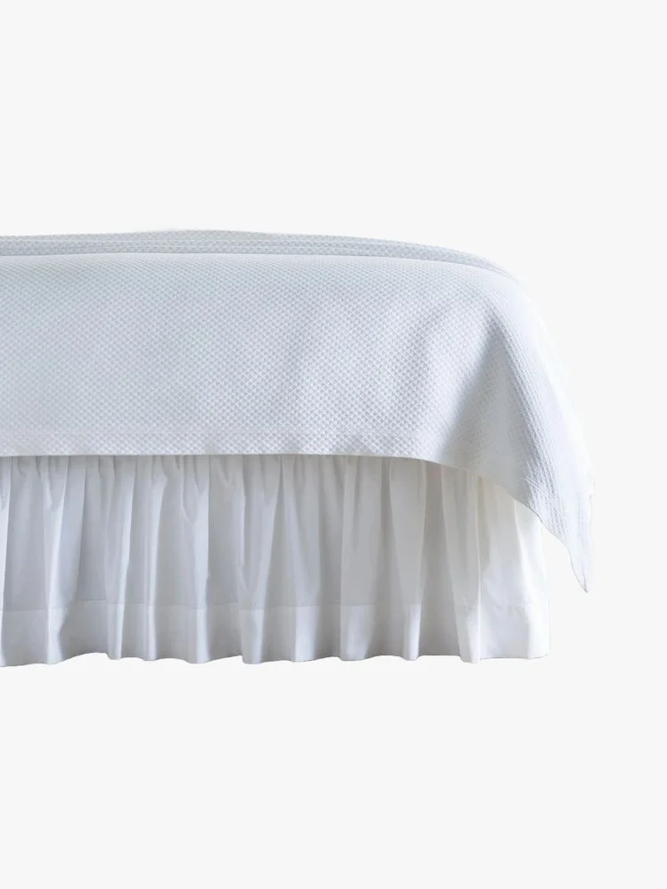 Bed with a white bed skirt on it.