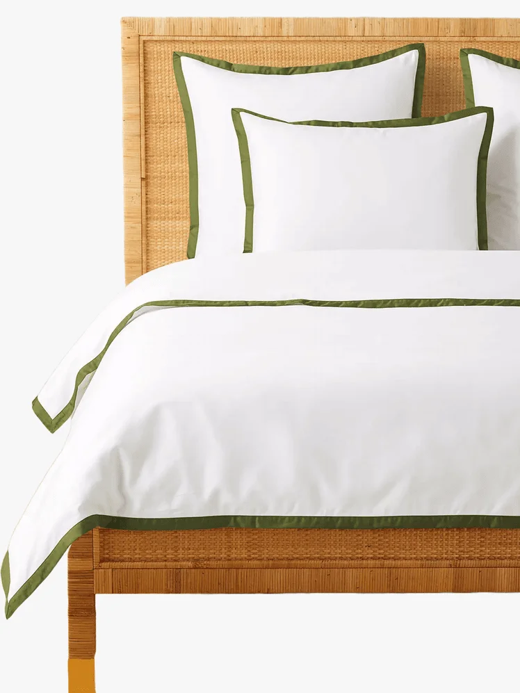 A white comforter and shams with green borders on a wooden bed