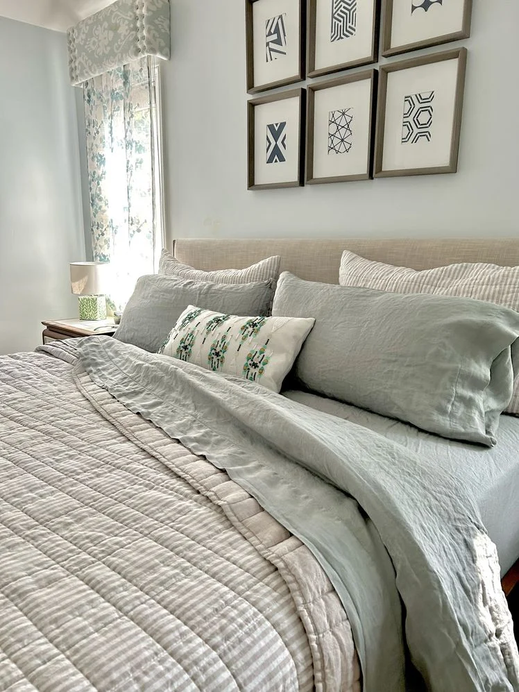 Bed made with light blue linen sheets and a striped comforter.