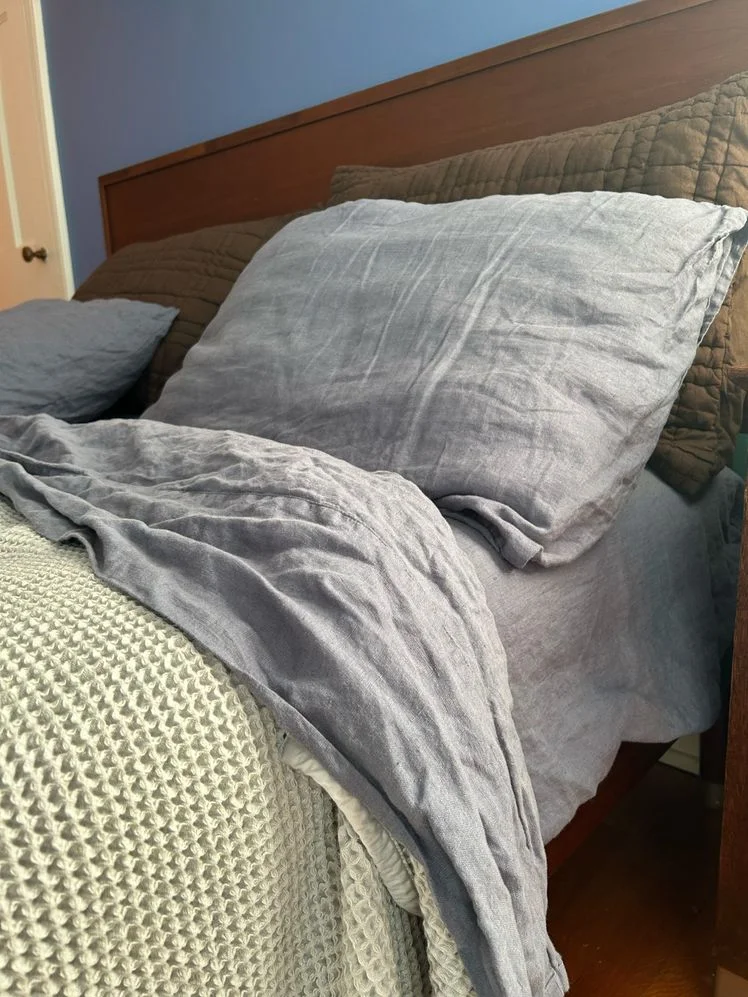 Bed made with light blue linen sheets and a green quilt.