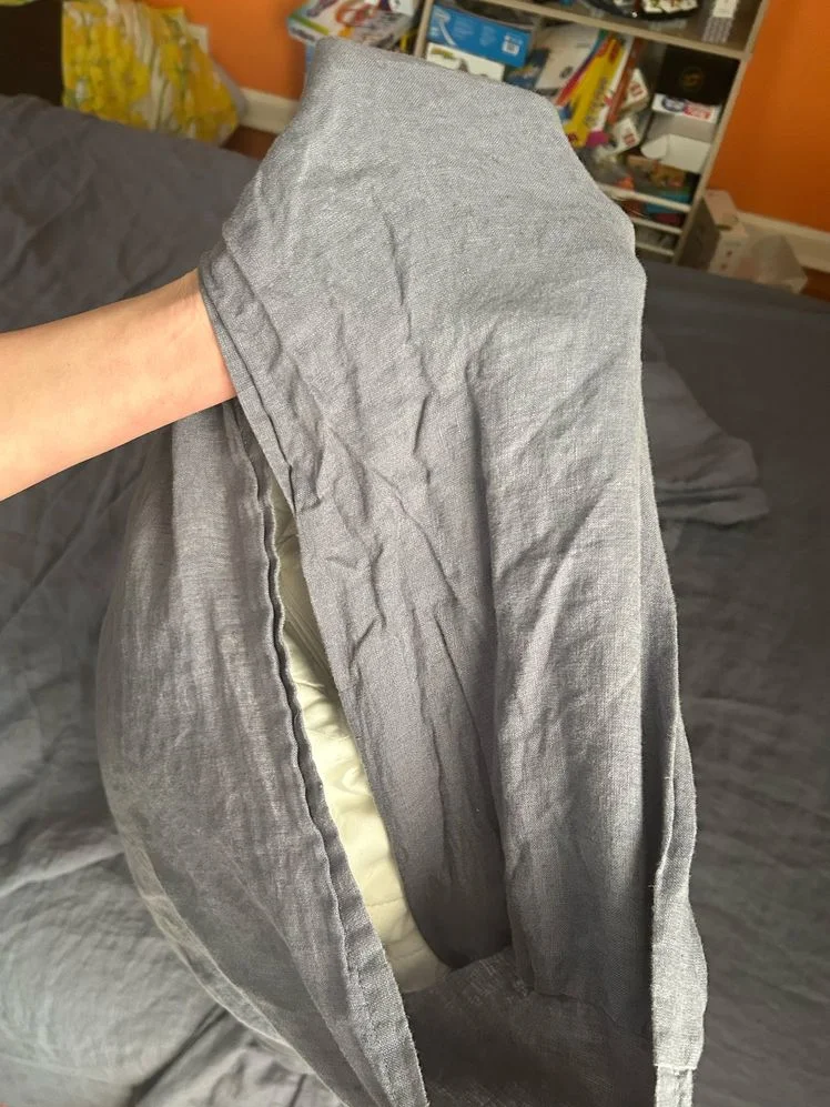 Person holding their hand through the center of a dusty blue linen pillowcase.