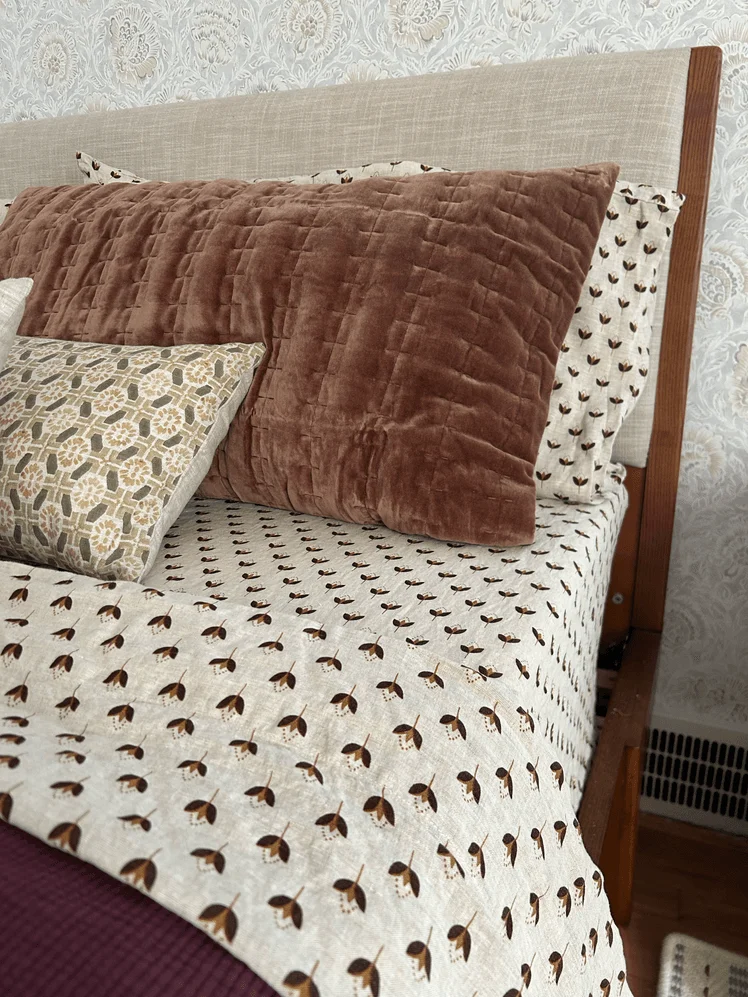 Bed made with patterned sheets and warm toned pillows.