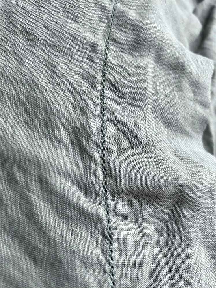 Closeup of embroidery on a set of light blue linen sheets.