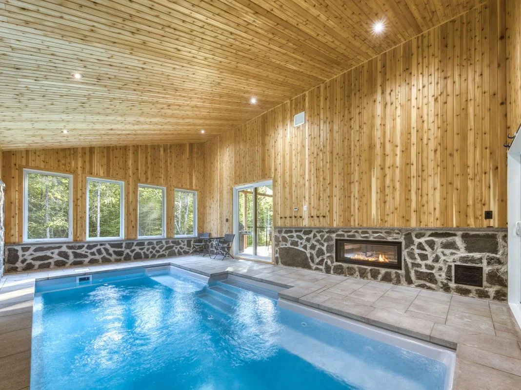 A pool sits in a room with a fireplace and exposed wood and stone features.