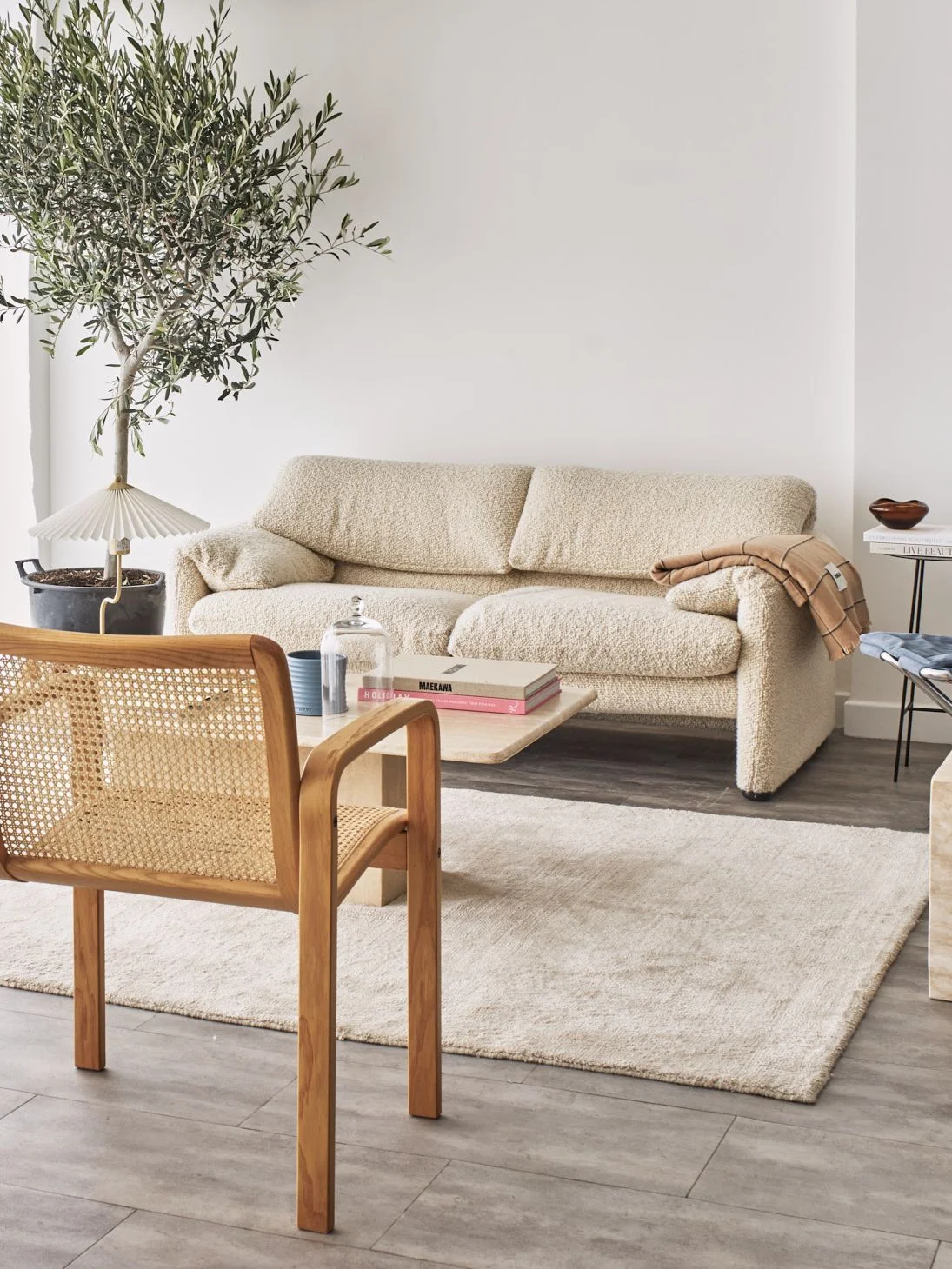 Beige boucle couh in a living room surrounded by rattan chairs and other light colored furnishings.