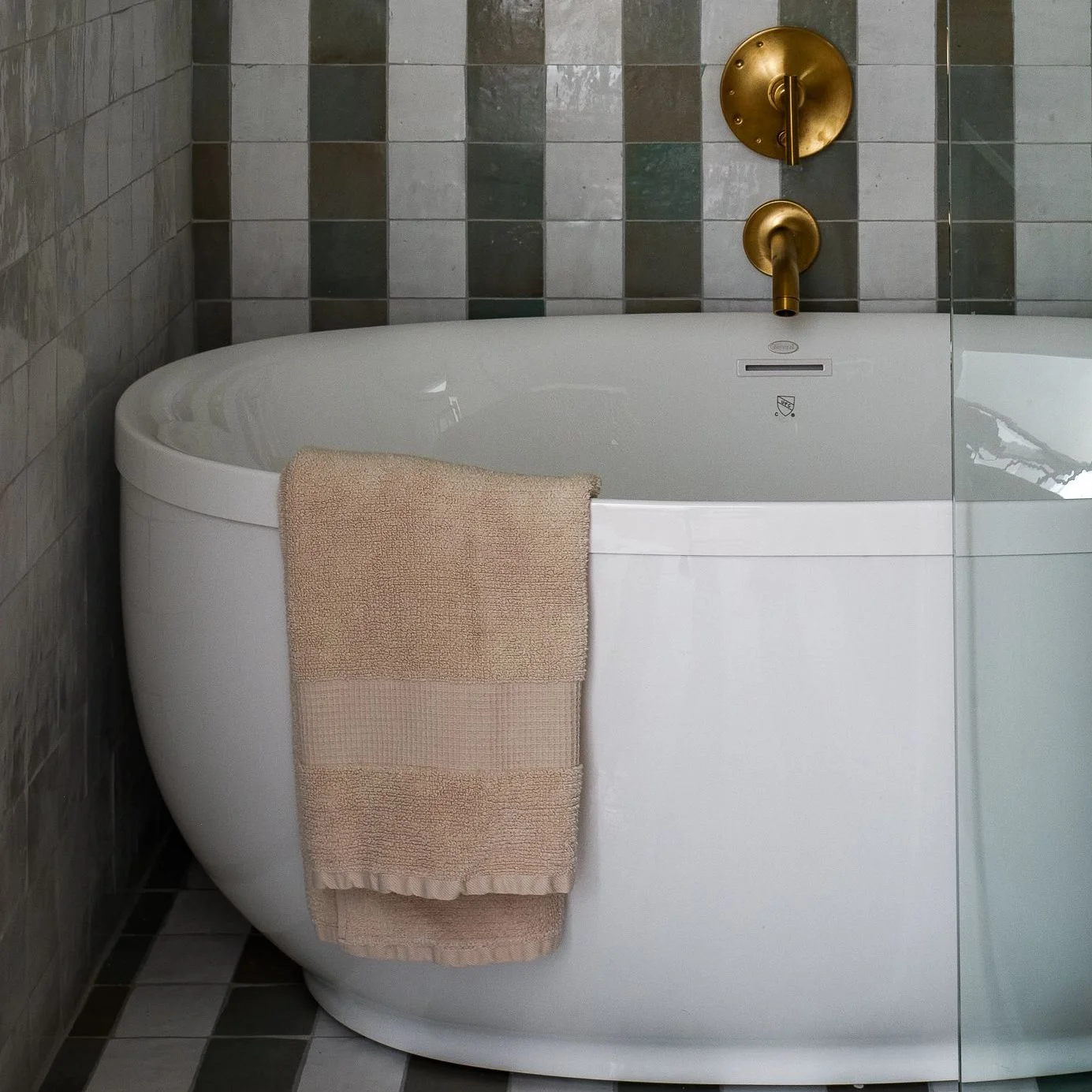 Bathroom with striped tile on walls and floor and a towel hanging over the edge of a bath tub.