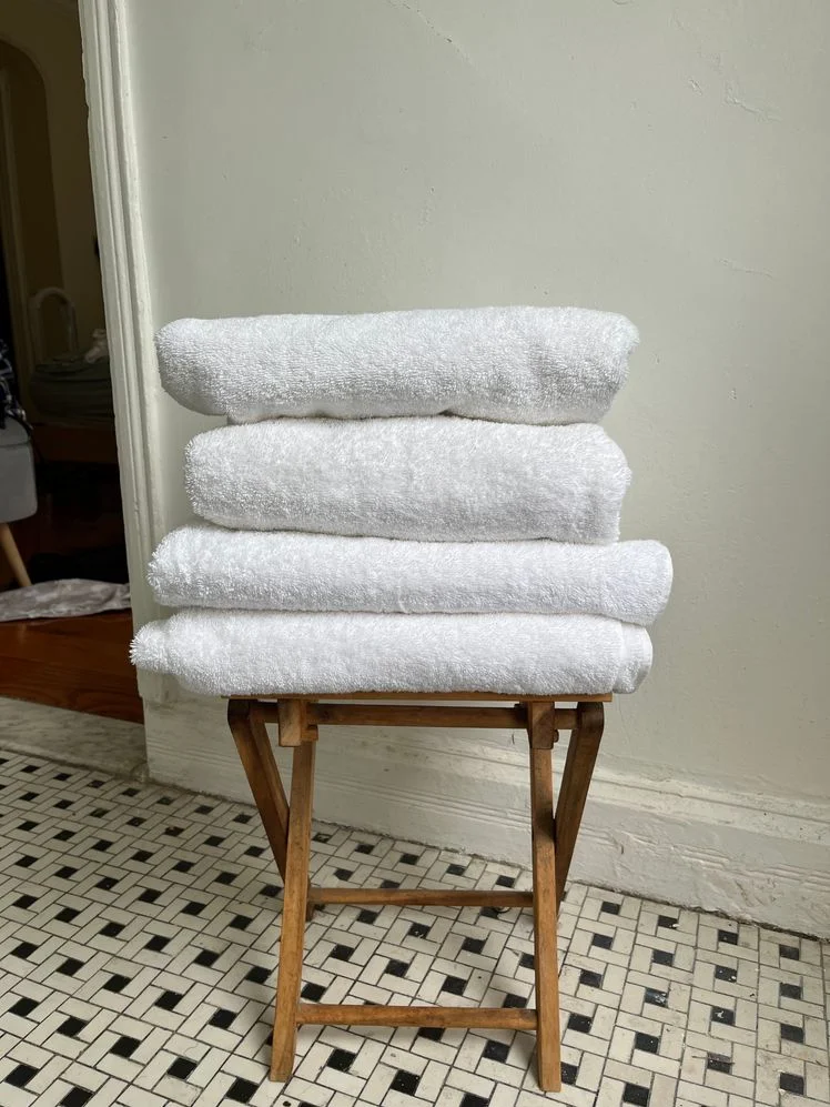 Stack of white folded towels on a wooden stool in a bathroom.