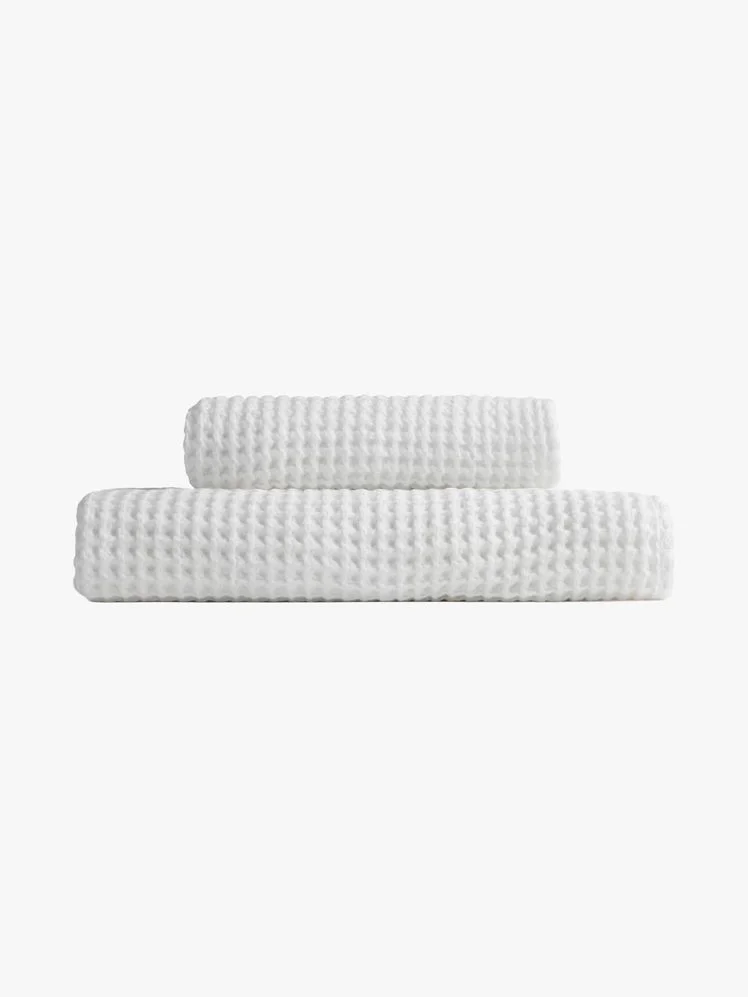 Two different size white waffle knit bath towels folded and stacked on top of each other.