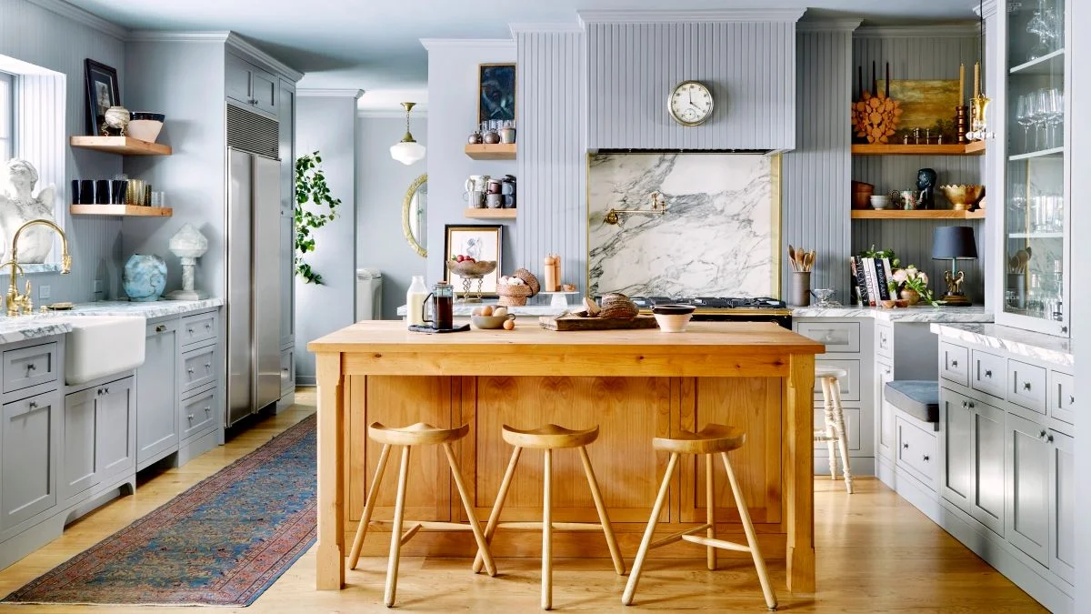 Gray paneled kitchen with marble countertops and a wooden island with matching stools.