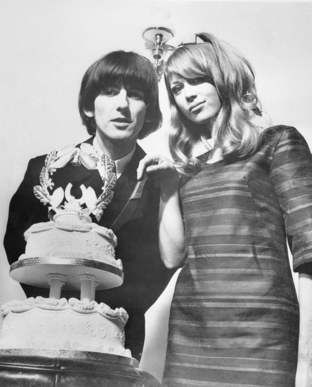 blackandwhite photo of George Harrison on wedding day left posed with Pattie Boyd and their multitired wedding cake
