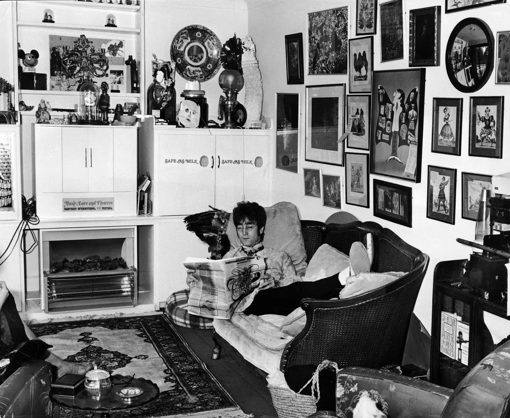 blackandwhite photo of John Lennon reading seated on sofa gallery wall to right fireplace to left