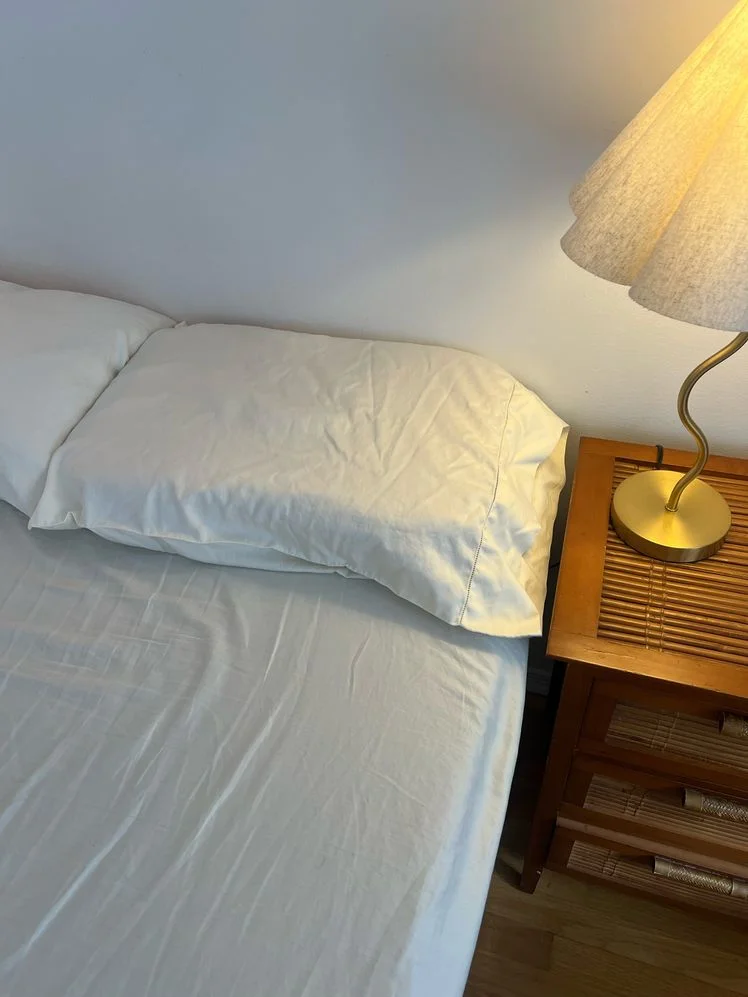 White sheets on a bed with a lamp on the bedside table.
