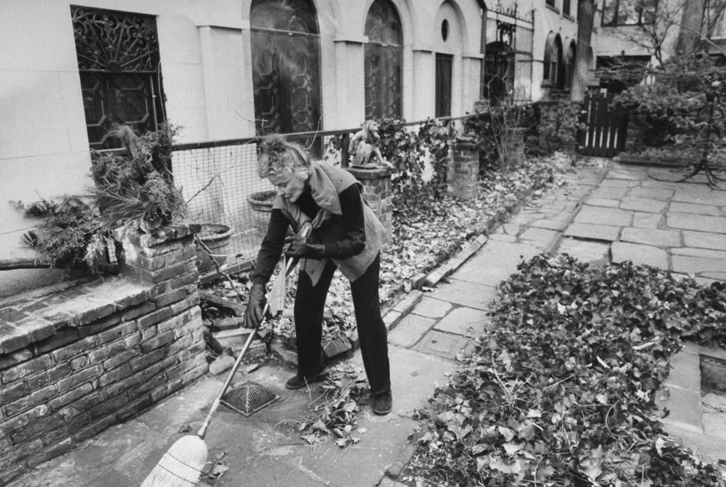 blackandwhite photo of Katharine Hepburn sweeping leaves on the patio of her New York City town house