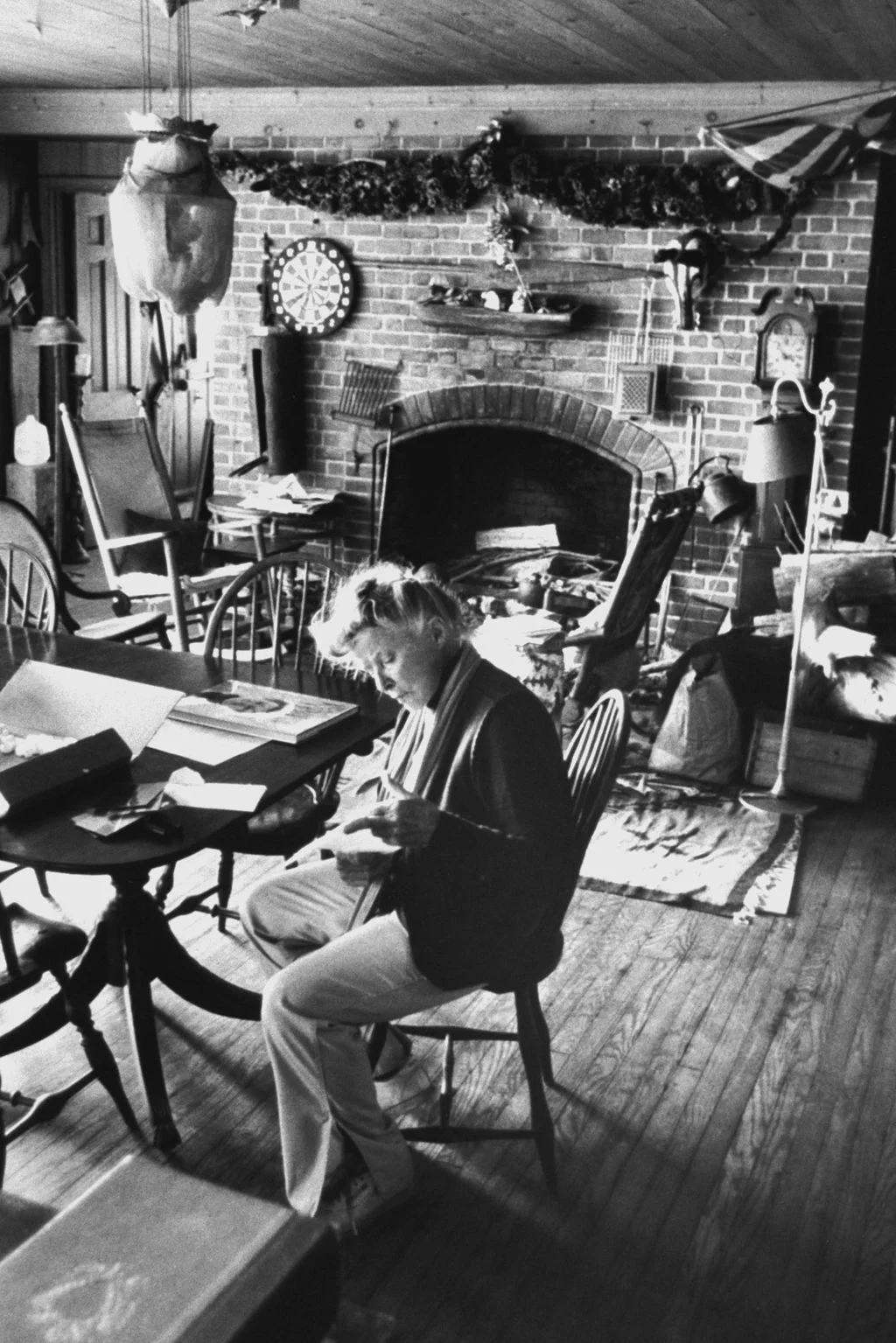 blackandwhite photo of Katharine Hepburn seated at table brick fireplace behind her