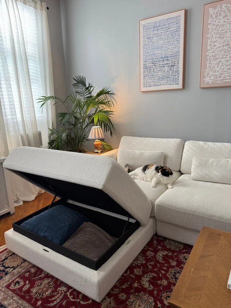 White couch with a matching storage ottoman, the ottoman hinged open.