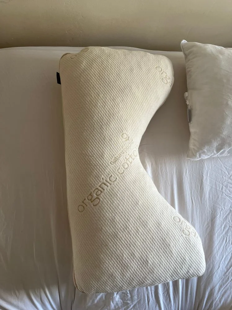 Bed pillow with a straight side and a curved side on a mattress.