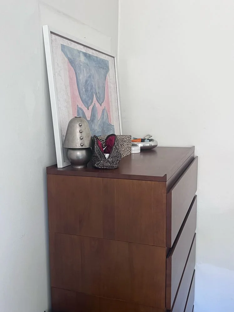 Thuma wood dresser shown from the side with a framed art piece, lamp, and assorted toiletries on top of it.