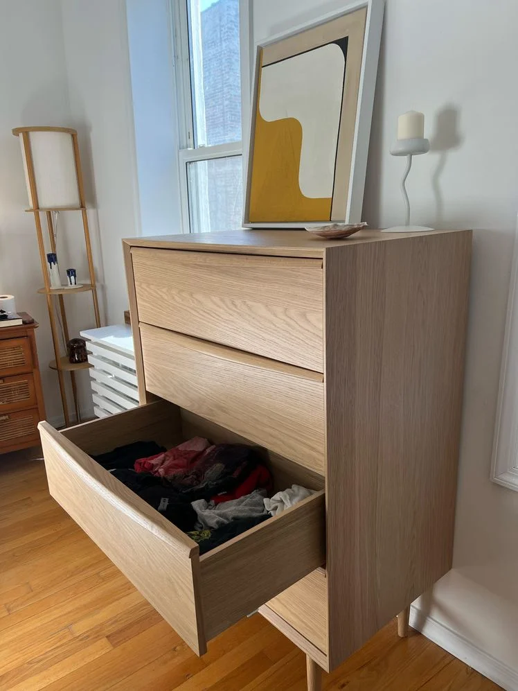 Wooden 4-drawer dresser shown from the side with a drawer open in a bedroom.