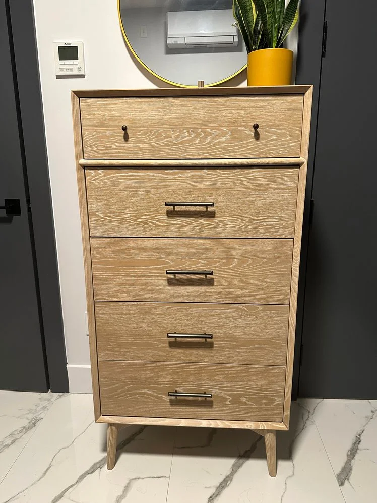Tall pale wood dresser on marble floor in a bedroom.