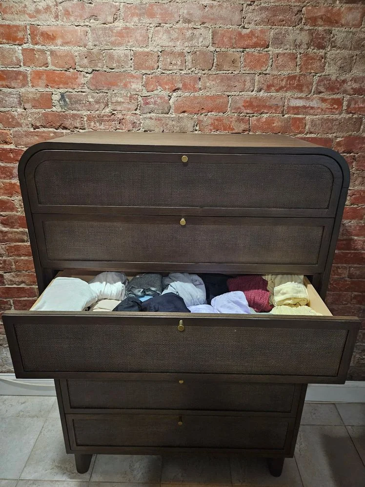 Brown wood dresser with gold hardware in front of a brick wall, with one drawer open.